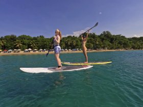 Two friends enjoy paddleboarding in clear waters near a beautiful beach, showcasing the fun and adventure of water activities.