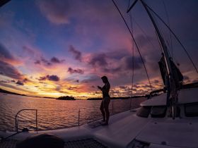 A silhouette of a woman enjoying a stunning sunset aboard a catamaran, capturing the essence of serene moments on the water.