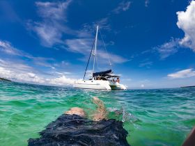 A stunning view of a catamaran anchored in crystal-clear waters, with a swimmer enjoying the vibrant underwater scenery — perfect for adventure seekers and water enthusiasts.