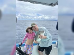 A joyful moment captured as a father and daughter proudly display their catch while fishing on the open ocean — a perfect family adventure.