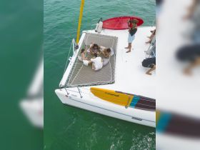 A lively group enjoys a relaxing moment on the netting of a catamaran, showcasing the perfect blend of fun and leisure on the water.
