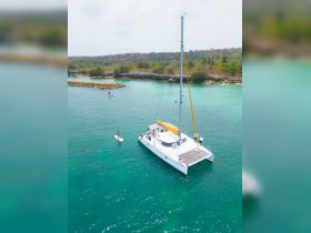 A scenic view of a catamaran anchored in turquoise waters, with a paddleboarder enjoying the beautiful surroundings — perfect for water sports enthusiasts.