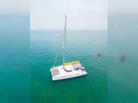 An aerial view of a catamaran sailing in clear turquoise waters, with guests enjoying water activities nearby, perfect for a day of adventure on the sea.