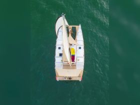 Aerial view of a catamaran sailing through clear waters, showcasing guests enjoying the deck — perfect for adventure seekers and sailing enthusiasts.