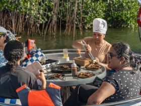 A group enjoys a delicious meal on a boat, showcasing a vibrant dining experience amidst the scenic mangroves — perfect for culinary adventures on the water.