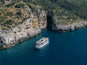 A scenic view of a tour boat navigating along a stunning coastline, showcasing the natural beauty of the cliffs and inviting waters — perfect for exploring hidden caves and enjoying the great outdoors.