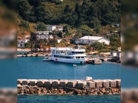 A scenic view of a boat docked in a tranquil harbor, surrounded by lush greenery and rustic buildings, perfect for exploring coastal destinations.