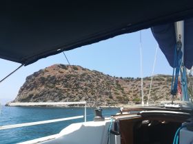 A serene view from the deck of a sailboat, showcasing a rocky coastline and clear blue waters — perfect for exploring hidden coves and enjoying the tranquility of the sea.