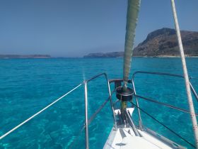 A stunning view from the bow of a sailboat cruising through crystal-clear turquoise waters, showcasing the beautiful coastline in the background.
