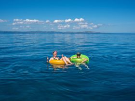 Two friends enjoy a sunny day floating in the ocean on colorful inflatable rings, showcasing the perfect atmosphere for relaxation and fun in the water.