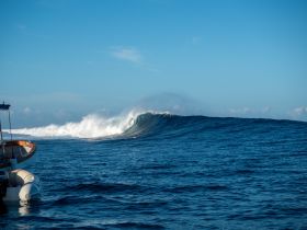 A stunning view of a surfer riding a massive wave, with a boat anchored nearby — capturing the thrill of ocean adventures.