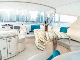 A stylish interior view of a boat's helm and seating area, featuring a decorative table and a backdrop of city skyscrapers, perfect for relaxing while cruising.