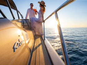 A couple enjoys cocktails on the deck of a yacht during a stunning sunset, creating the perfect romantic atmosphere for a memorable evening on the water.