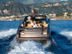 A couple relaxes on the deck of a sleek boat while cruising through stunning coastal scenery, perfect for a luxurious day on the water.
