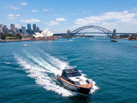 A stunning aerial view of a yacht cruising through the vibrant waters of Sydney, with the iconic Sydney Opera House and Harbour Bridge in the background, showcasing the beauty of the city.