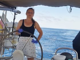 A woman navigates the helm of a sailboat, showcasing the thrill of sailing on open waters — perfect for adventure seekers and sailing enthusiasts.