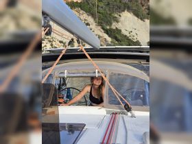 A woman smiles from the helm of a sailboat, showcasing the cozy interior space designed for navigation and relaxation on the water.