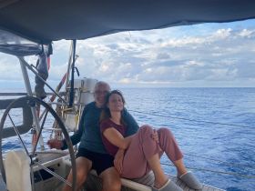 A couple enjoys a serene moment aboard a sailboat, surrounded by the vast ocean — perfect for romantic getaways and sailing adventures.