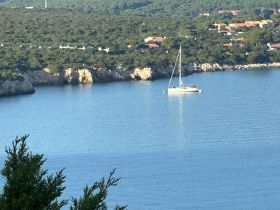 A serene view of a sailboat anchored in calm waters, surrounded by lush greenery and rocky cliffs, perfect for showcasing tranquil boating experiences.