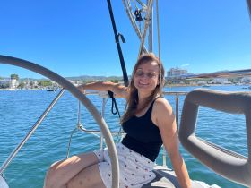 A woman enjoys a sunny day on a boat, smiling against a picturesque harbor backdrop — perfect for relaxing outings on the water.