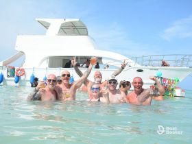 A lively group enjoys a fun day in the water, celebrating with cocktails and laughter, with a beautiful boat in the background — perfect for memorable outings.