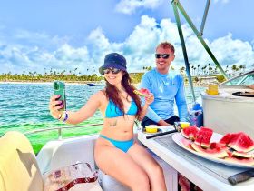 A joyful moment captured as a woman takes a selfie while enjoying watermelon with a friend on a boat — perfect for summer outings and fun on the water.