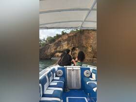 A couple enjoys the scenic view from the back of a boat, overlooking a stunning rock formation — a perfect moment for adventure seekers exploring the coastline.