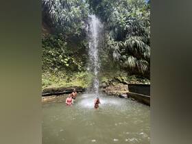 A group enjoys a refreshing swim under a stunning waterfall, surrounded by lush greenery — a perfect nature escape.