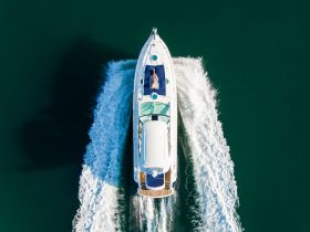 A stunning aerial view of a yacht cruising through clear waters, showcasing its sleek design and vibrant wake — perfect for luxury boating experiences.