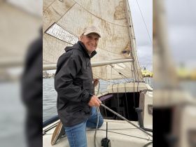 A smiling man actively sailing a boat, showcasing the joy of navigating the waters. Perfect for those looking to capture the essence of sailing adventures.