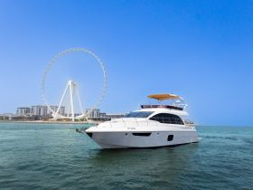 A stunning yacht cruising in clear waters, with a backdrop of a large Ferris wheel and modern buildings, perfect for showcasing luxury boating experiences.