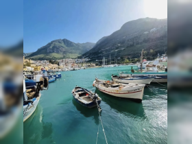 A picturesque view of fishing boats docked in a serene harbor, surrounded by lush mountains and clear turquoise waters, perfect for exploring coastal destinations.