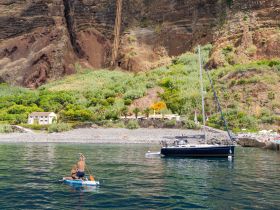 A couple enjoys paddleboarding in calm waters with a scenic backdrop of cliffs and a beach, showcasing the perfect blend of adventure and relaxation.