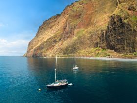 A stunning aerial view of two sailboats anchored near a dramatic coastline, showcasing the natural beauty of the landscape and tranquil waters.