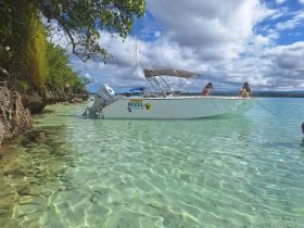 Two friends relax on the bow of a boat anchored in crystal-clear waters, surrounded by stunning natural scenery — a perfect spot for a day of fun and relaxation.