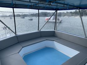 A cozy seating area inside a boat, featuring comfortable cushions and a view of the water through large windows, perfect for relaxing while cruising.