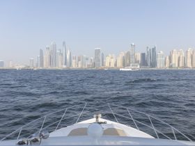 A stunning view from the bow of a yacht cruising through the waters of Dubai, showcasing the impressive skyline of the city in the background.
