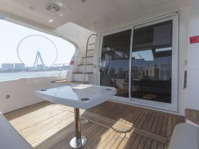 A stylish interior view of a boat featuring a sleek table and staircase, with a stunning backdrop of a Ferris wheel and city skyline visible through the large windows.