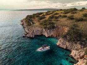 An aerial view captures a boat anchored near a stunning coastline, surrounded by crystal-clear turquoise waters — a perfect spot for relaxation and exploration.