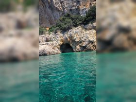 A stunning view of a rocky coastline featuring a cave entrance, surrounded by crystal-clear turquoise waters — a perfect destination for exploration and adventure.