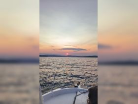 A serene sunset view from the bow of a boat, showcasing the tranquil waters and distant mountains — perfect for evening cruises and relaxation on the water.
