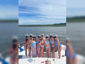 A lively group of friends celebrates aboard a boat, dressed in matching outfits and captain hats, perfect for a bachelorette party or summer getaway on the water.
