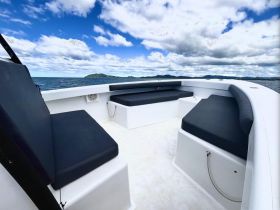 Interior view of a boat's seating area, showcasing comfortable black cushions against a backdrop of serene waters and a cloudy sky.