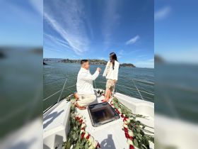 A romantic proposal takes place on a boat, surrounded by rose petals and a stunning waterfront backdrop — a perfect moment for couples celebrating love.