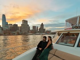 A couple enjoys a romantic moment on a yacht against the stunning backdrop of a city skyline at sunset, perfect for memorable evening cruises.