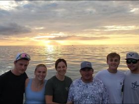 A cheerful group poses together against a stunning sunset backdrop, capturing a memorable moment on the water — perfect for family gatherings or friends' outings.