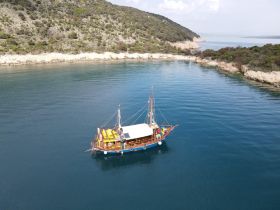 Aerial view of a beautifully crafted boat anchored in calm waters, surrounded by lush greenery and rocky coastline — perfect for exploring serene destinations.