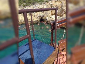 Guests enjoy swimming in crystal-clear waters near a rocky coast, creating a perfect backdrop for a fun day on the water.