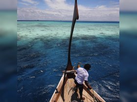 A crew member navigates a traditional boat over stunning turquoise waters, showcasing the beauty of tropical marine environments — perfect for adventure seekers and nature lovers.