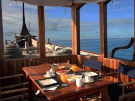 A beautifully arranged dining area inside a boat, featuring a breakfast spread with fresh fruits and drinks, perfect for enjoying meals while cruising on the water.
